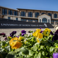 Flowers in the foreground with a building and "University of North Texas at Frisco" signage in the background.