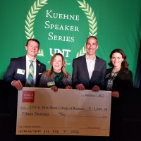 Four individuals stand behind a large ceremonial check for $15,000. The event appears to be part of the "Kuehne Speaker Series" at UNT.
